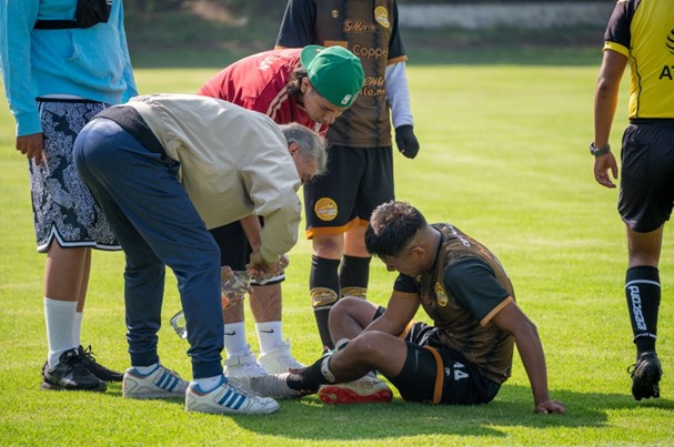 football player injured on the field holding his leg with emergency medical around